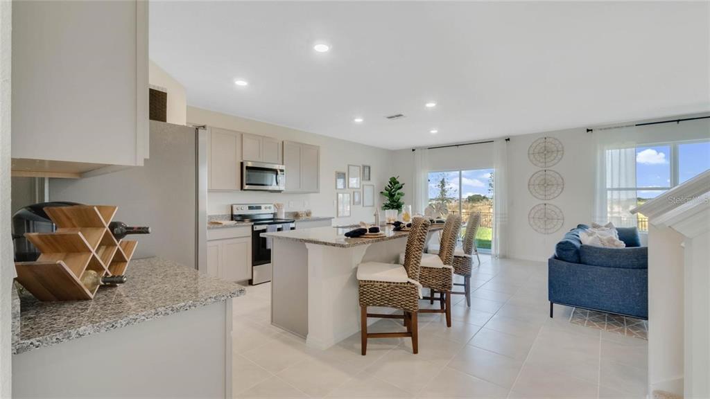 An open-concept kitchen and living area features a granite island, wicker stools, and tile flooring — 572 LAKE WILDMERE COVE, LONGWOOD, FL