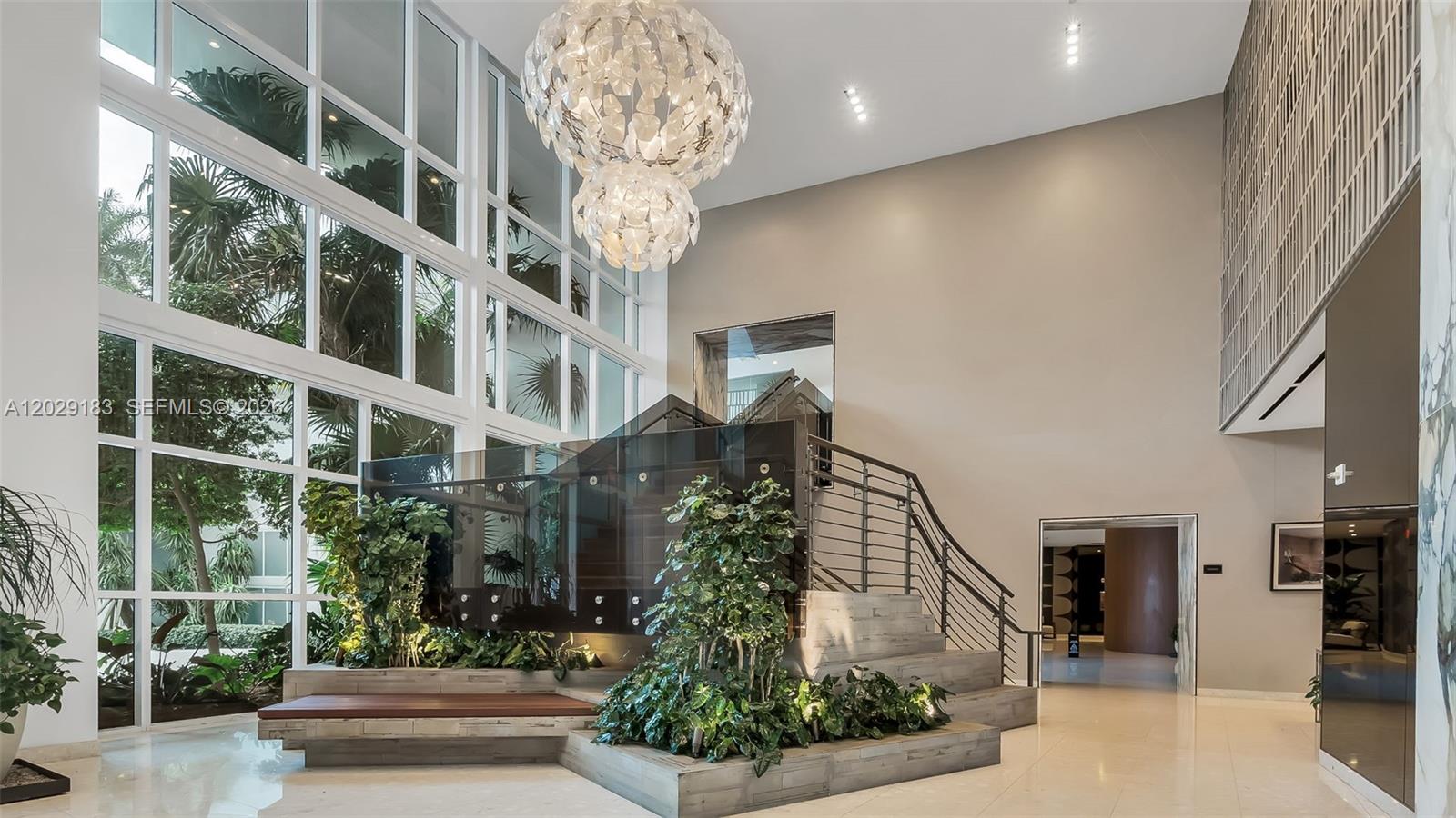 A modern lobby features a grand staircase, a large chandelier, and indoor planters — 2020 N Bayshore Dr # 2603, Miami FL 33137, MIAMI, FL