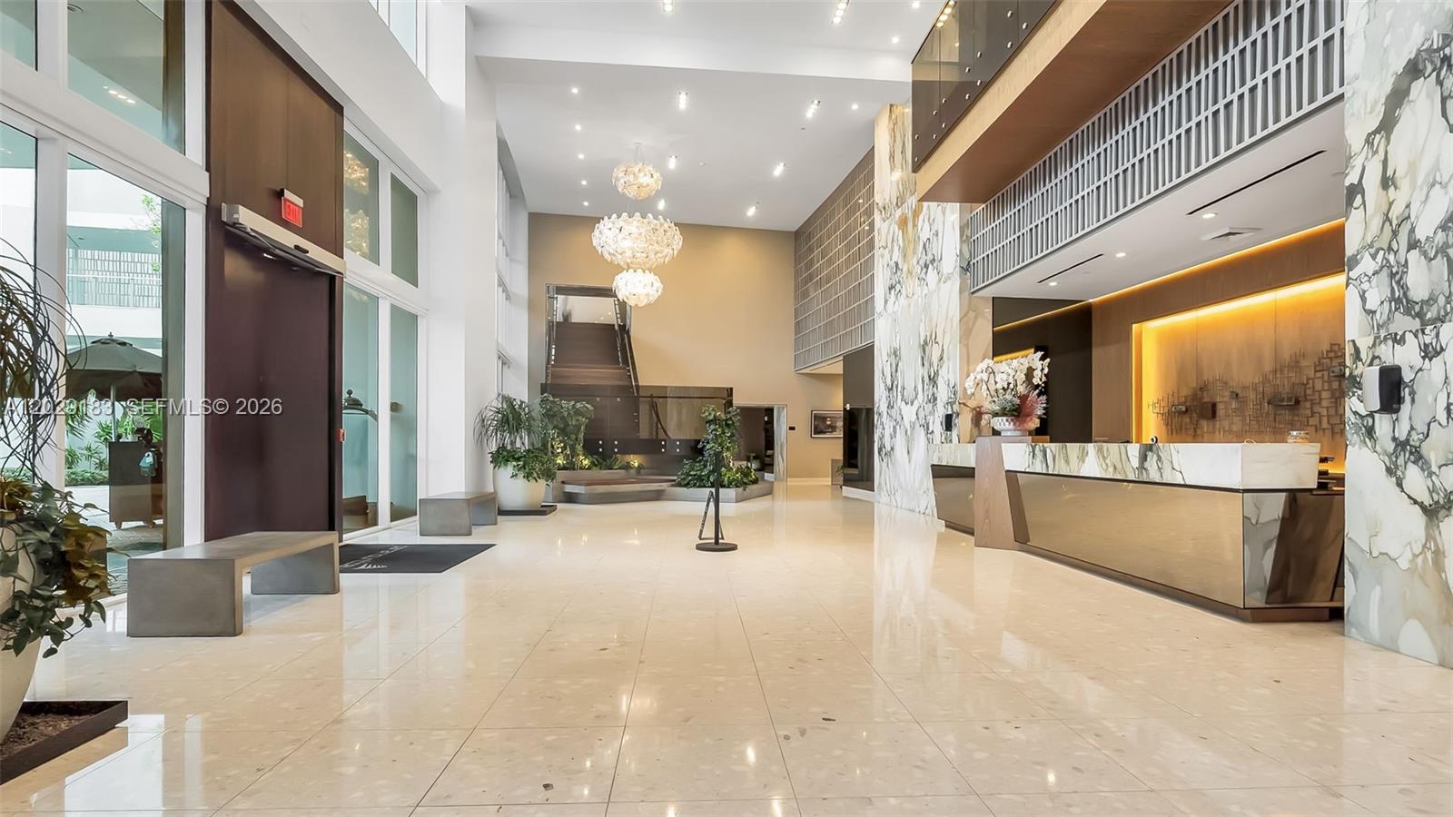 A modern building lobby features a marble reception desk, high ceilings, and a grand chandelier — 2020 N Bayshore Dr # 2603, Miami FL 33137, MIAMI, FL