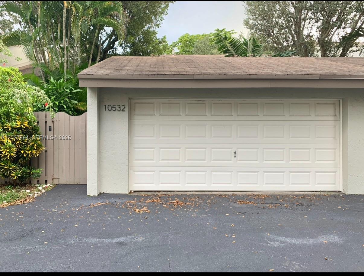 A white garage door with a brown shingled roof and a wooden gate nearby — 10532 SW 112th Ave, Miami FL 33176, MIAMI, FL