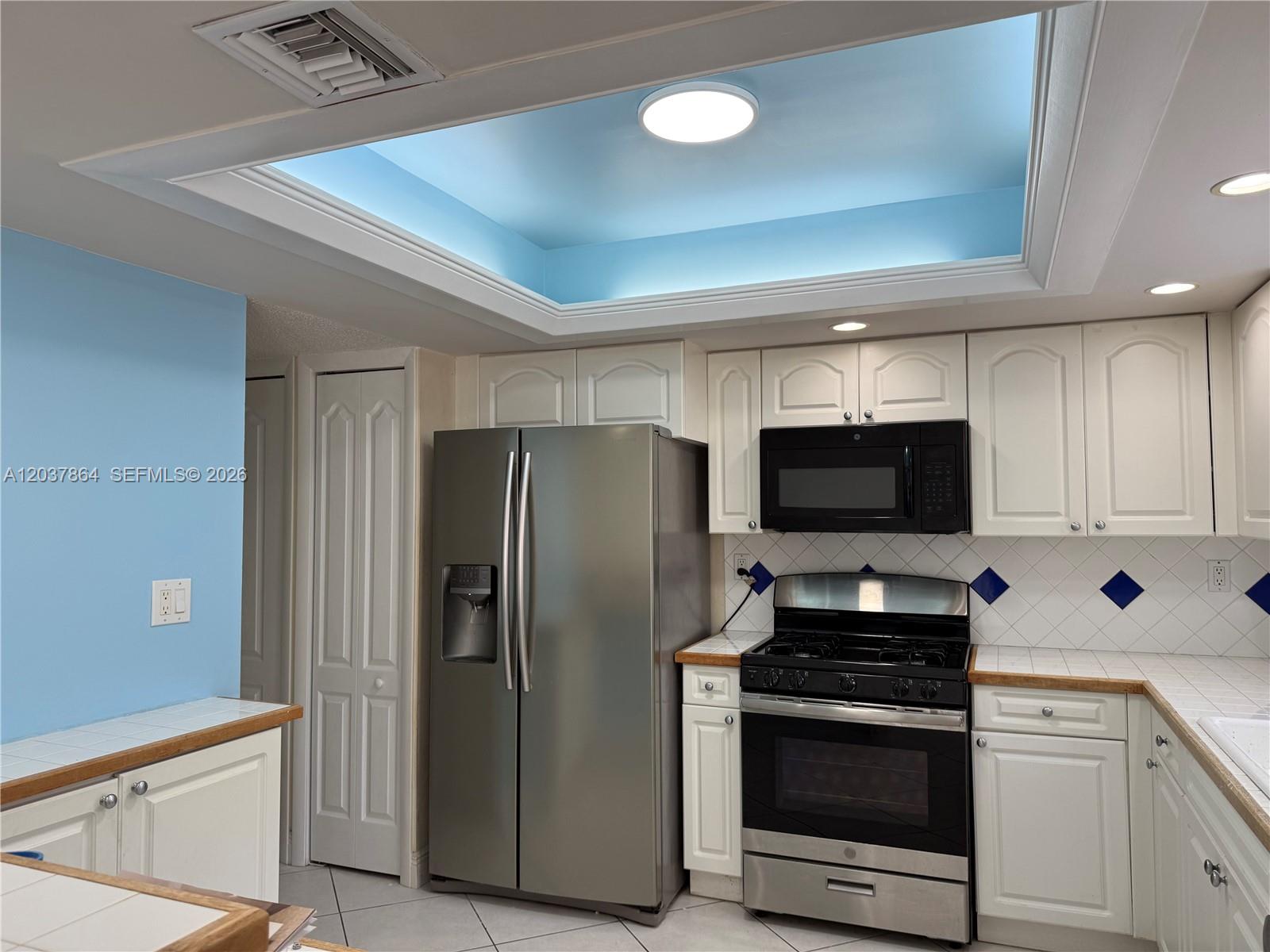 A kitchen features white cabinets, stainless steel appliances, a blue tray ceiling, and tiled countertops — 10532 SW 112th Ave, Miami FL 33176, MIAMI, FL