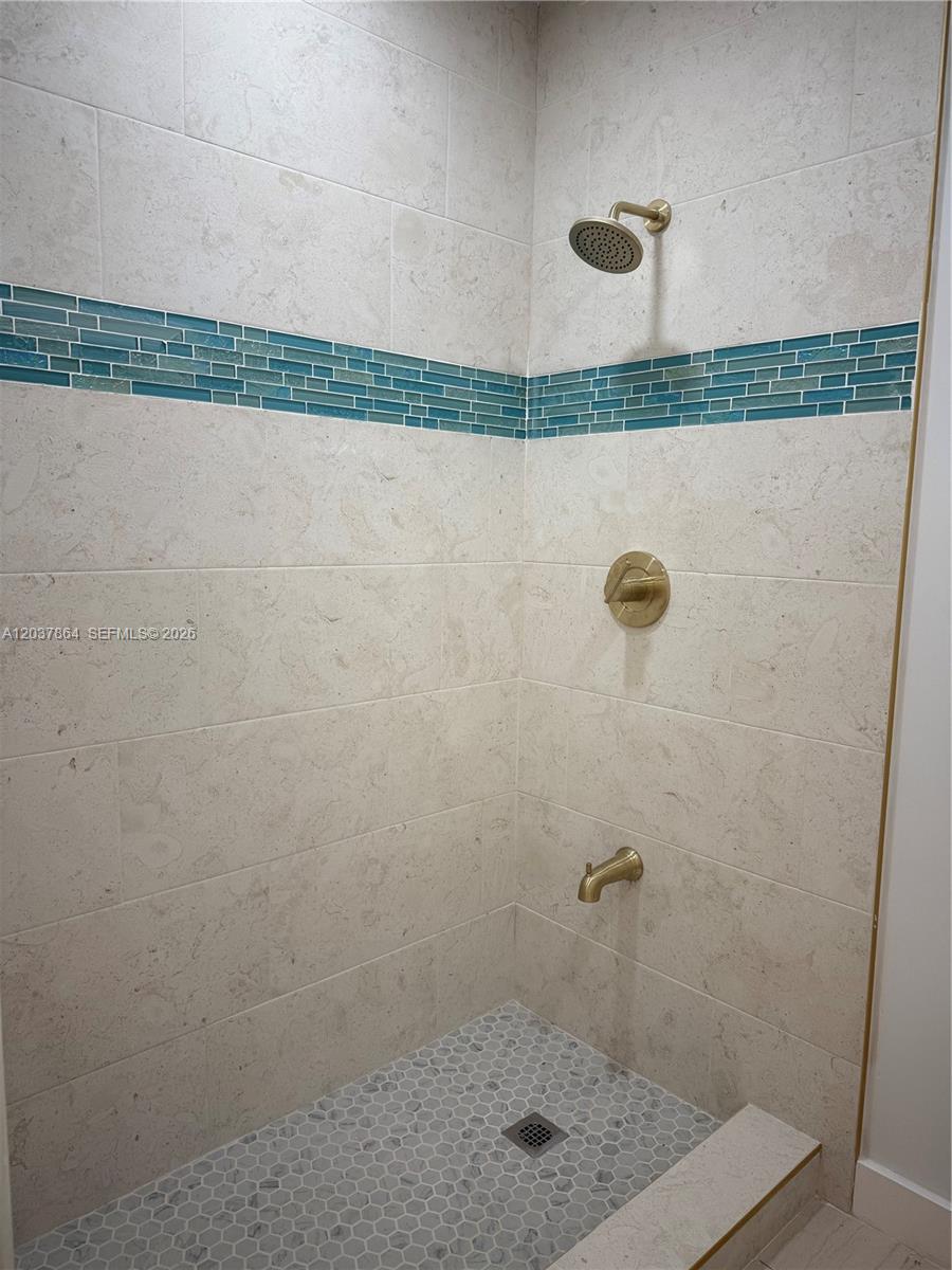 A walk-in shower features light-colored stone wall tiles, a blue glass accent strip, and brass fixtures — 10532 SW 112th Ave, Miami FL 33176, MIAMI, FL