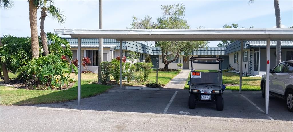 A covered carport sits in front of a single-story residential building with a golf cart — 1811 BEDFORD LANE UNIT 157, SUN CITY CENTER, FL