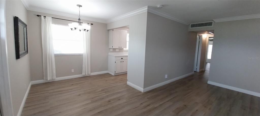 A dining area with wood-look flooring, white cabinets, and a chandelier next to a hallway — 1811 BEDFORD LANE UNIT 157, SUN CITY CENTER, FL