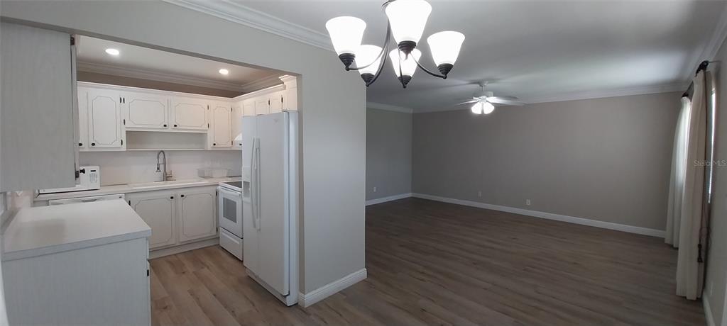 A kitchen with white cabinets and appliances opens into a spacious living area with wood-look flooring — 1811 BEDFORD LANE UNIT 157, SUN CITY CENTER, FL