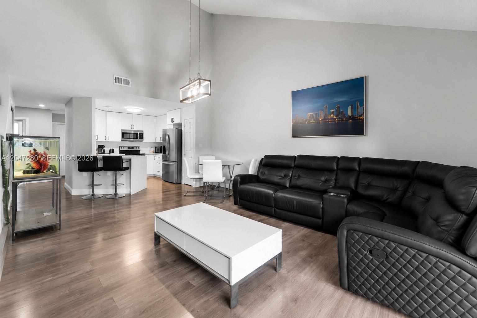 A living room with a black sectional sofa, white coffee table, and an open kitchen — 12909 SW 64th Ln, Miami FL 33183, MIAMI, FL