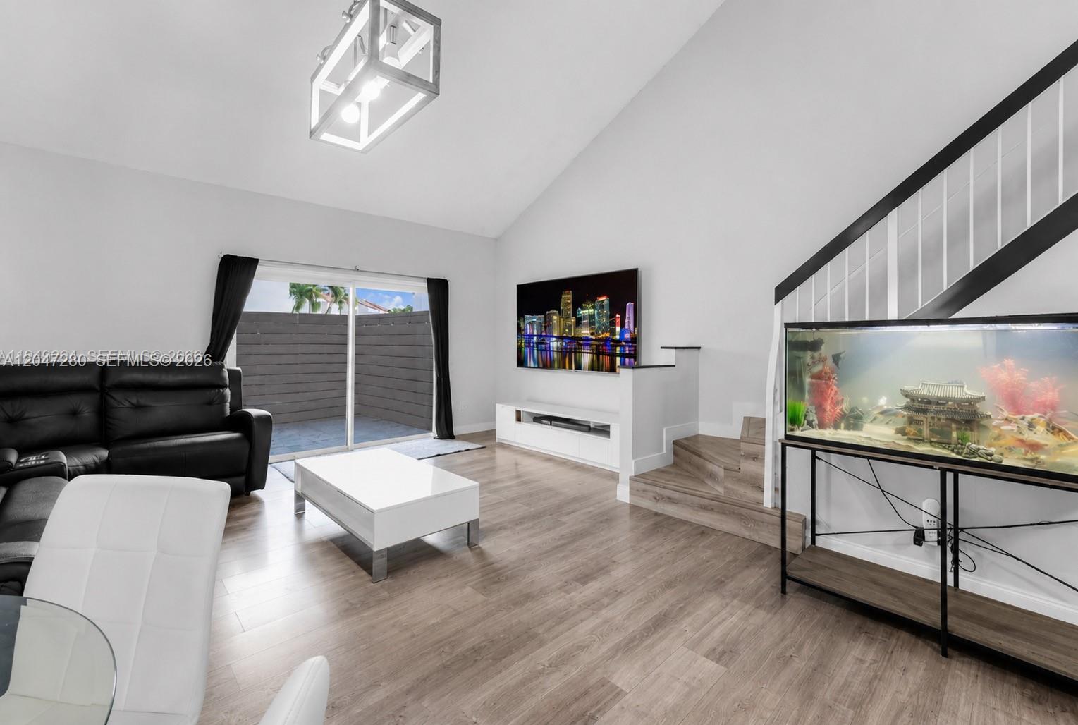 A living room features wood-look flooring, a vaulted ceiling, a fish tank, and sliding glass doors — 12909 SW 64th Ln, Miami FL 33183, MIAMI, FL
