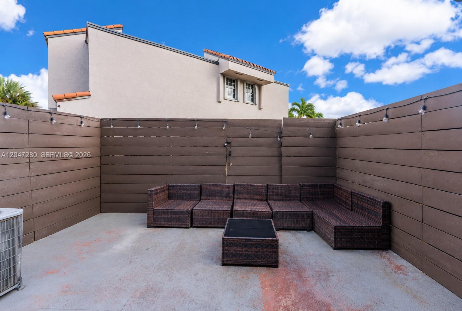A patio features a modular wicker sofa, a matching coffee table, and a wooden fence — 12909 SW 64th Ln, Miami FL 33183, MIAMI, FL