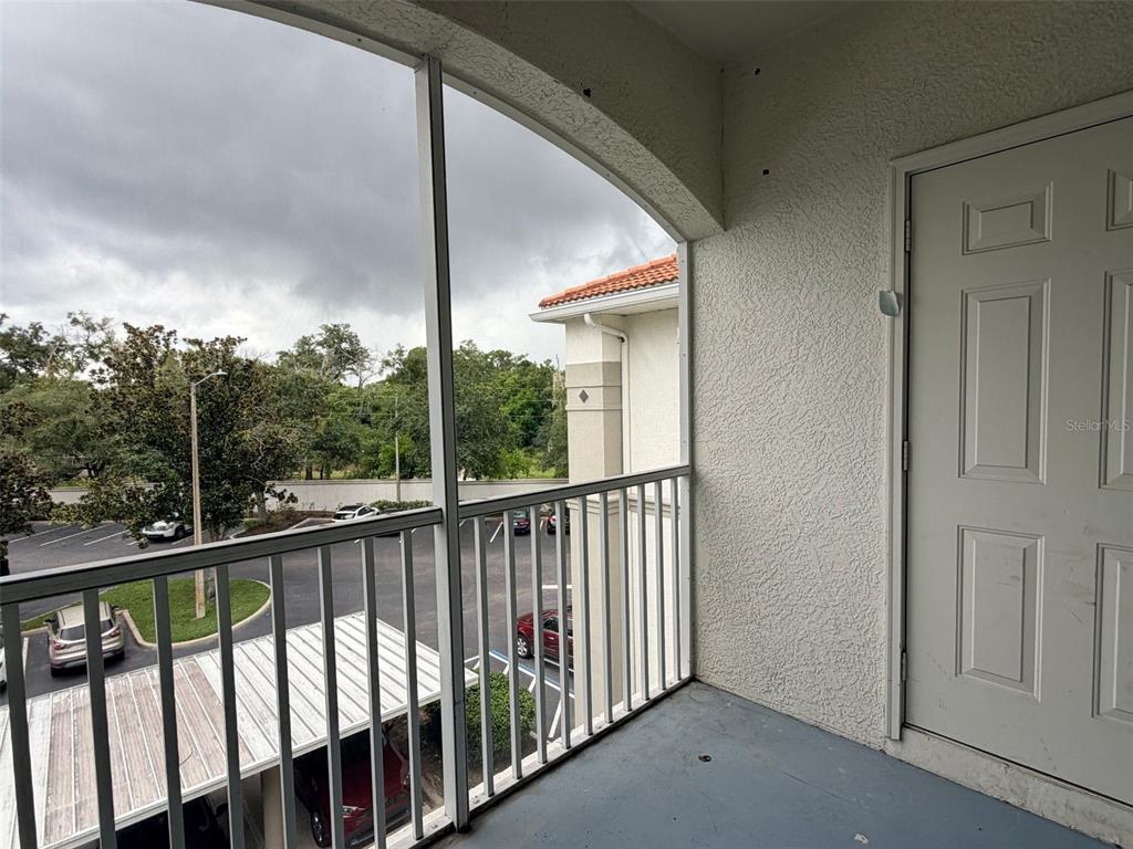 A screened-in balcony overlooks a parking lot with covered carports and surrounding trees — 2651 MAITLAND CROSSING WAY UNIT 303, ORLANDO, FL