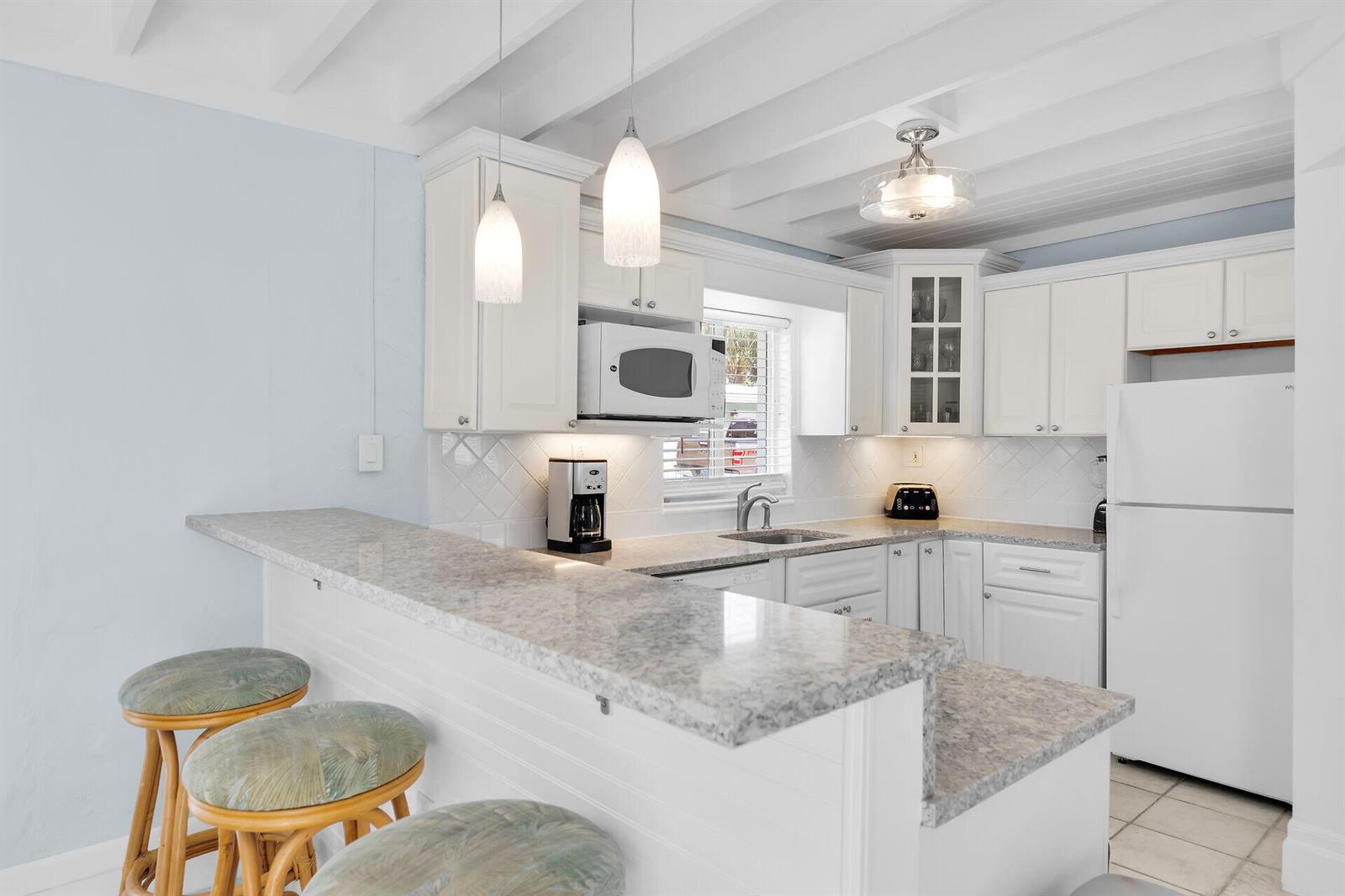 A kitchen features white cabinets, granite countertops, a breakfast bar with stools, and exposed beams — 11725 3rd Avenue Ocean, Marathon FL 33050, MARATHON, FL