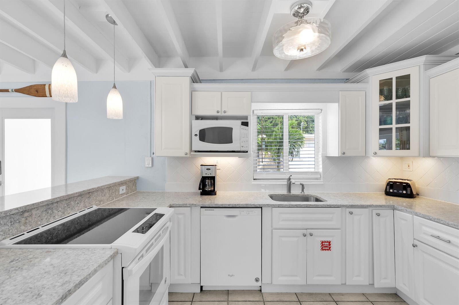 A white kitchen features granite countertops, white cabinetry, a dishwasher, and a window above the sink — 11725 3rd Avenue Ocean, Marathon FL 33050, MARATHON, FL