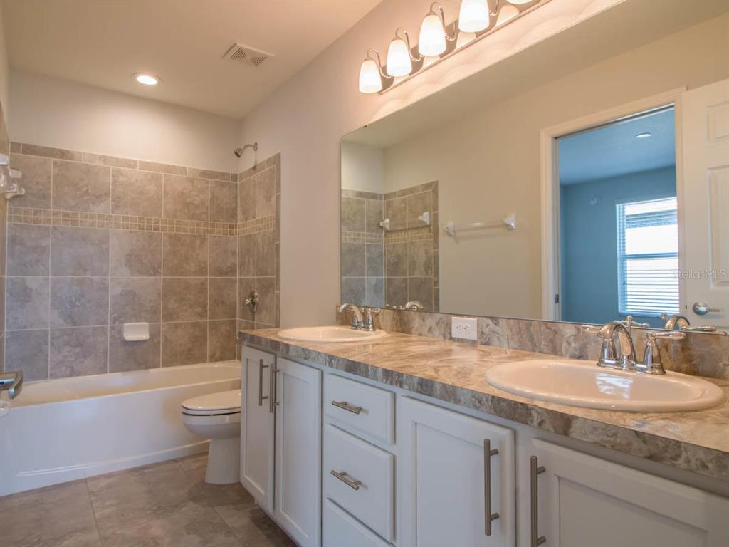A bathroom features a double vanity with stone countertops, white cabinets, and a tiled tub — 1097 GRANTHAM DRIVE, SARASOTA, FL