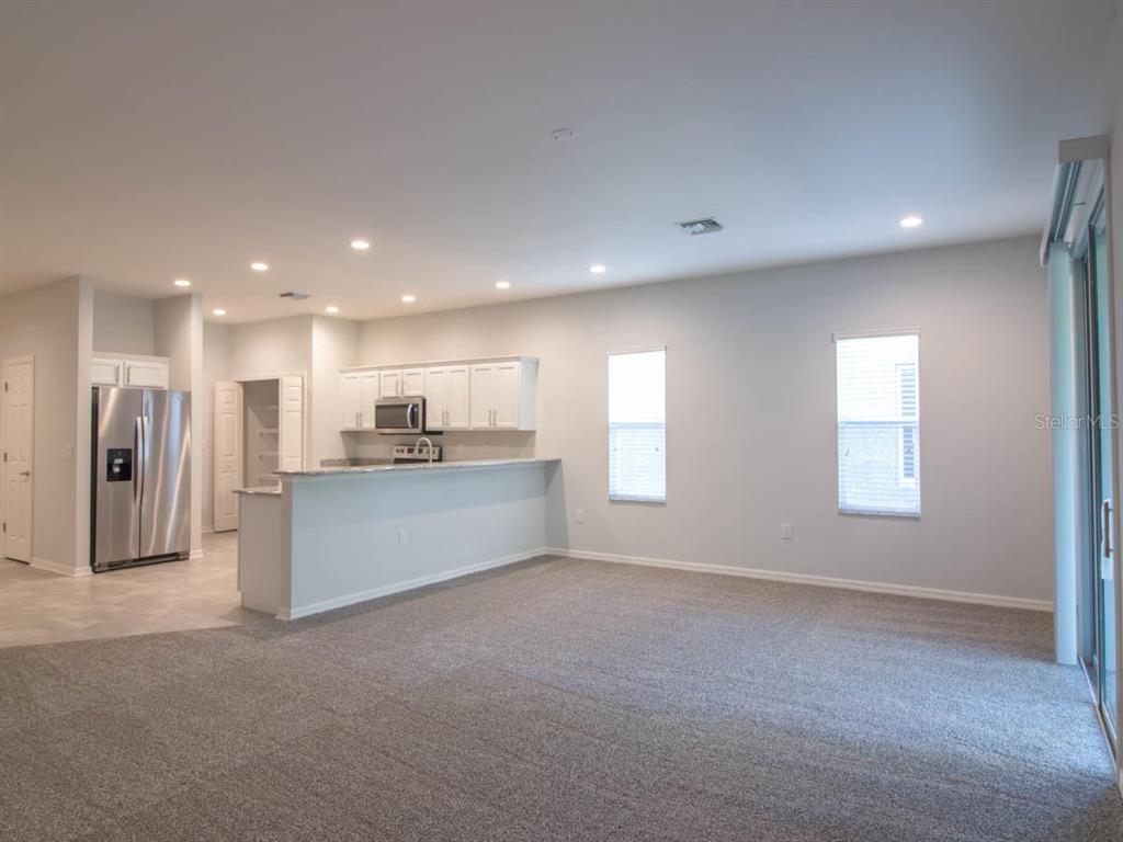 An open-concept kitchen with white cabinets and a breakfast bar overlooks a carpeted living area — 1097 GRANTHAM DRIVE, SARASOTA, FL