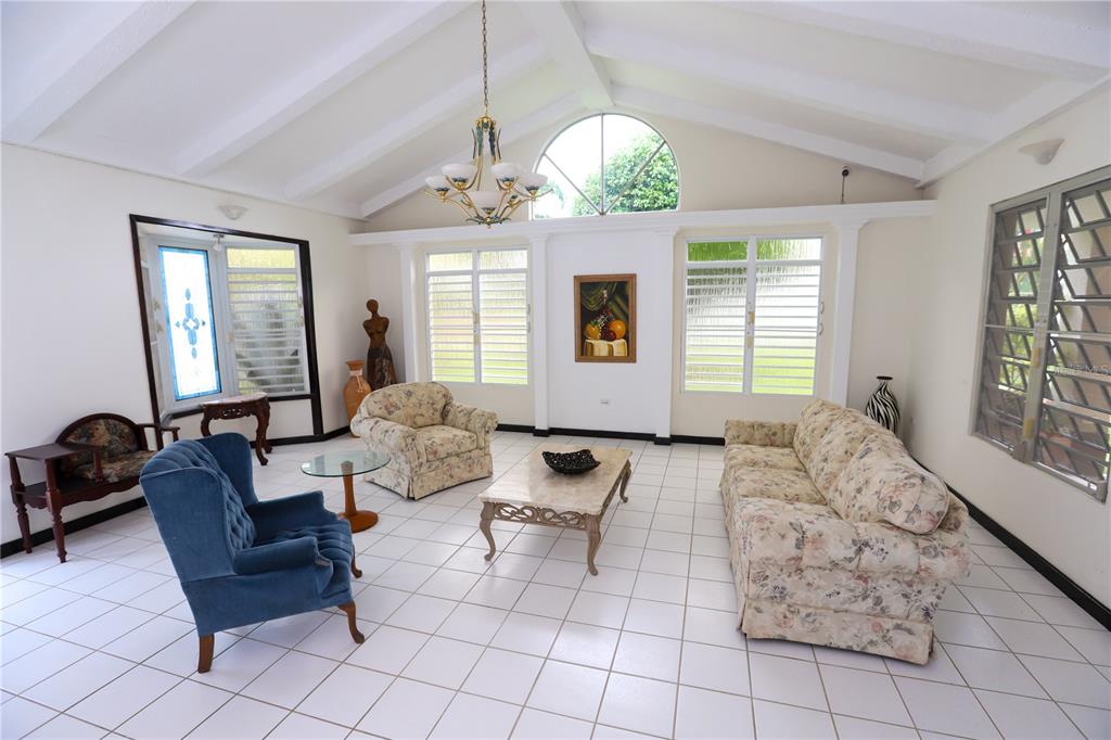 A bright living room features white tiled floors, vaulted ceilings, and floral-patterned furniture — FINQUITAS DEL MONTE, CIDRA, PR