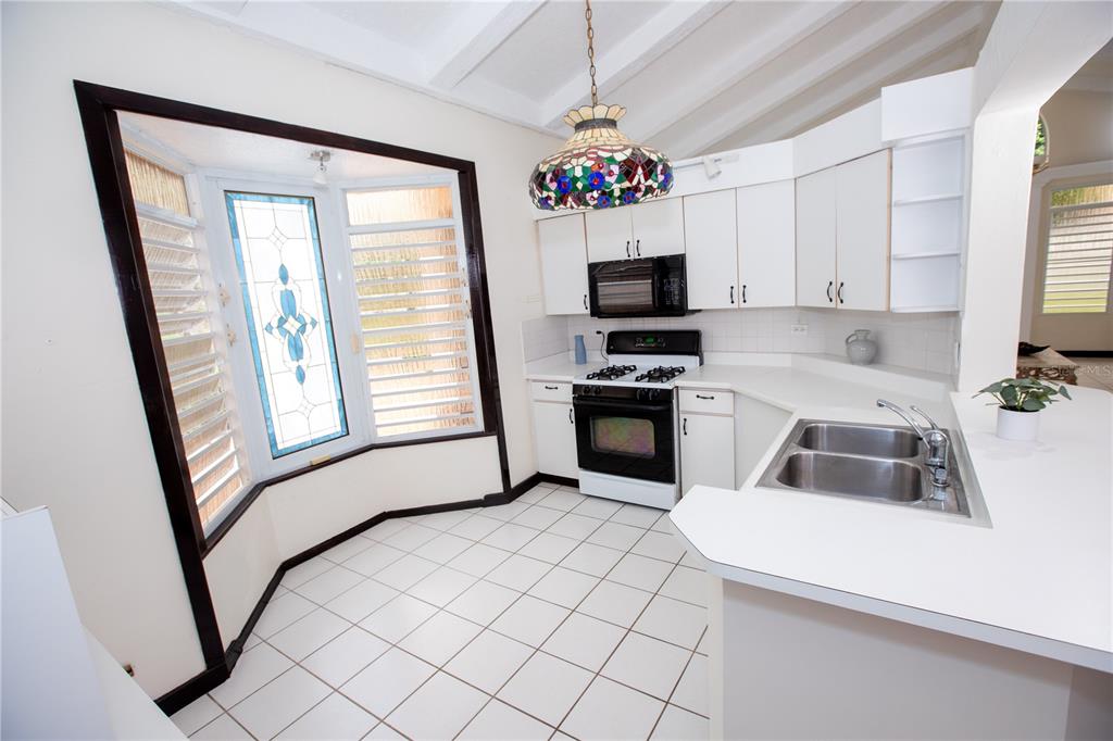 A kitchen features white cabinets, a gas stove, a double sink, and a bay window — FINQUITAS DEL MONTE, CIDRA, PR