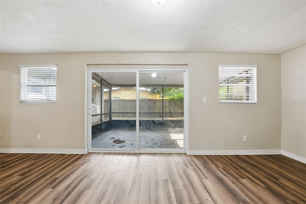 A room with wood-look flooring, two windows, and a sliding glass door to a screened porch — 4132 WESTGATE ROAD, ORLANDO, FL