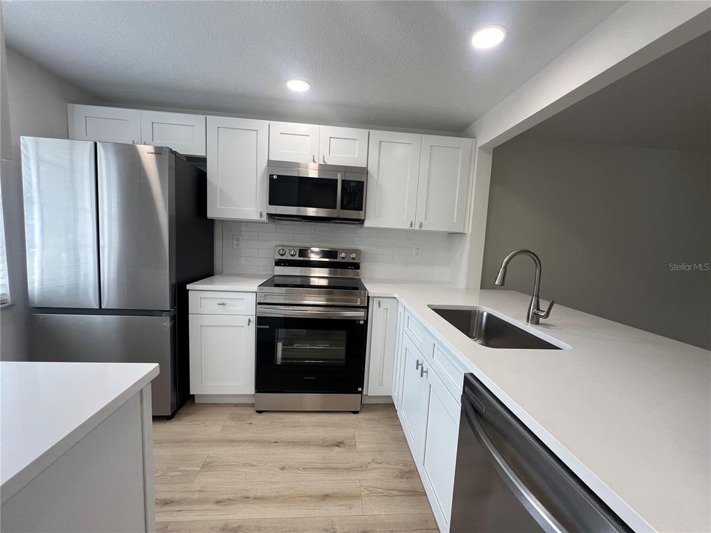 A modern kitchen features white cabinets, stainless steel appliances, and light wood-look flooring — 4223 SHELDON PLACE UNIT 23, NEW PORT RICHEY, FL