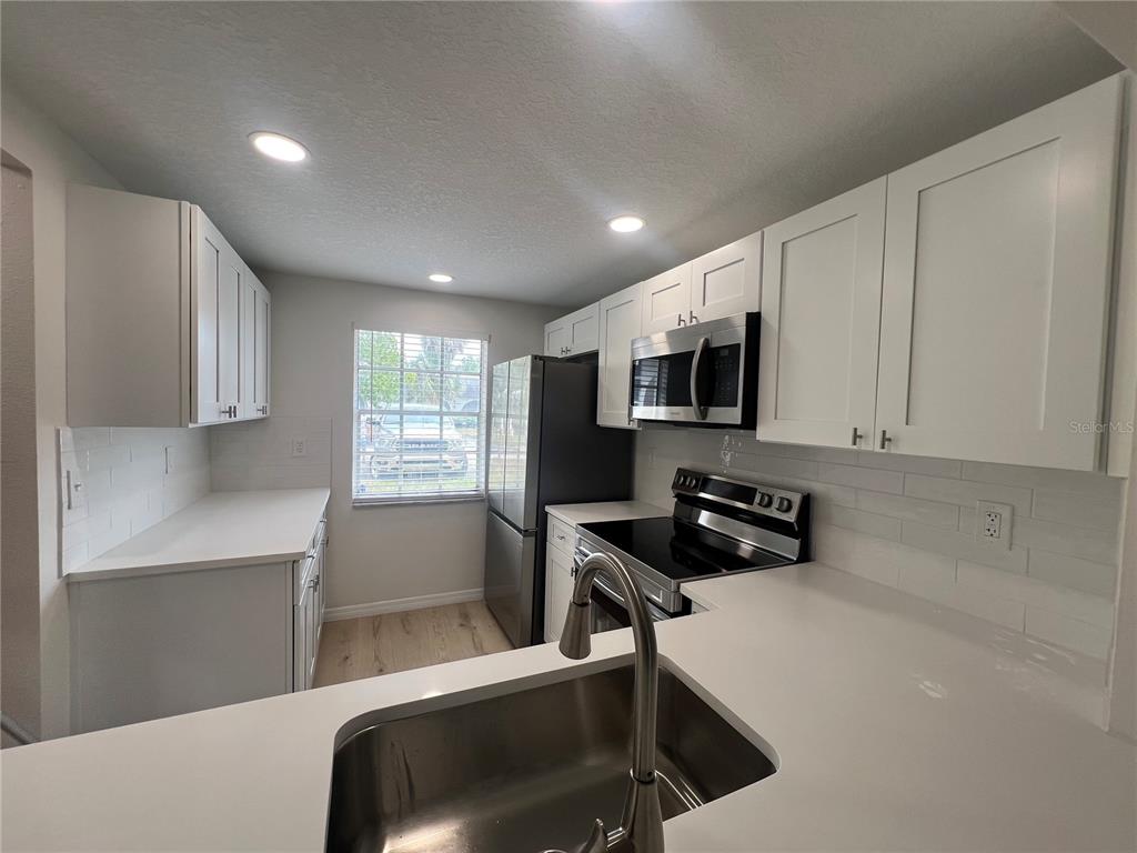 A kitchen with white cabinets, stainless steel appliances, a sink, and light-colored countertops — 4223 SHELDON PLACE UNIT 23, NEW PORT RICHEY, FL