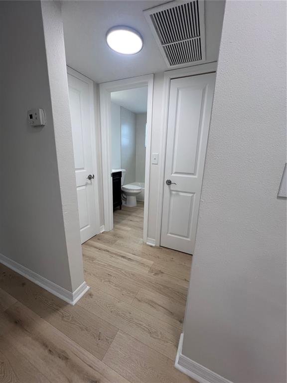 A hallway with light wood flooring leads to a bathroom with a toilet and tub — 4223 SHELDON PLACE UNIT 23, NEW PORT RICHEY, FL
