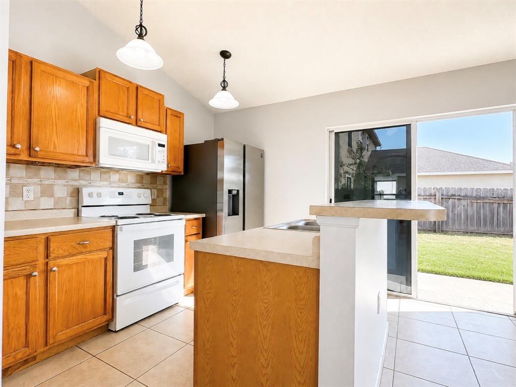 A kitchen features oak cabinets, white appliances, a center island, and a sliding glass door — 508 POINTE ALLYSON WAY, ORLANDO, FL