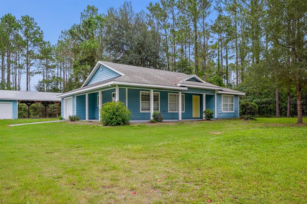A blue single-story house with a covered porch and an adjacent carport sits on grass — 670 SW 105TH STREET, TRENTON, FL