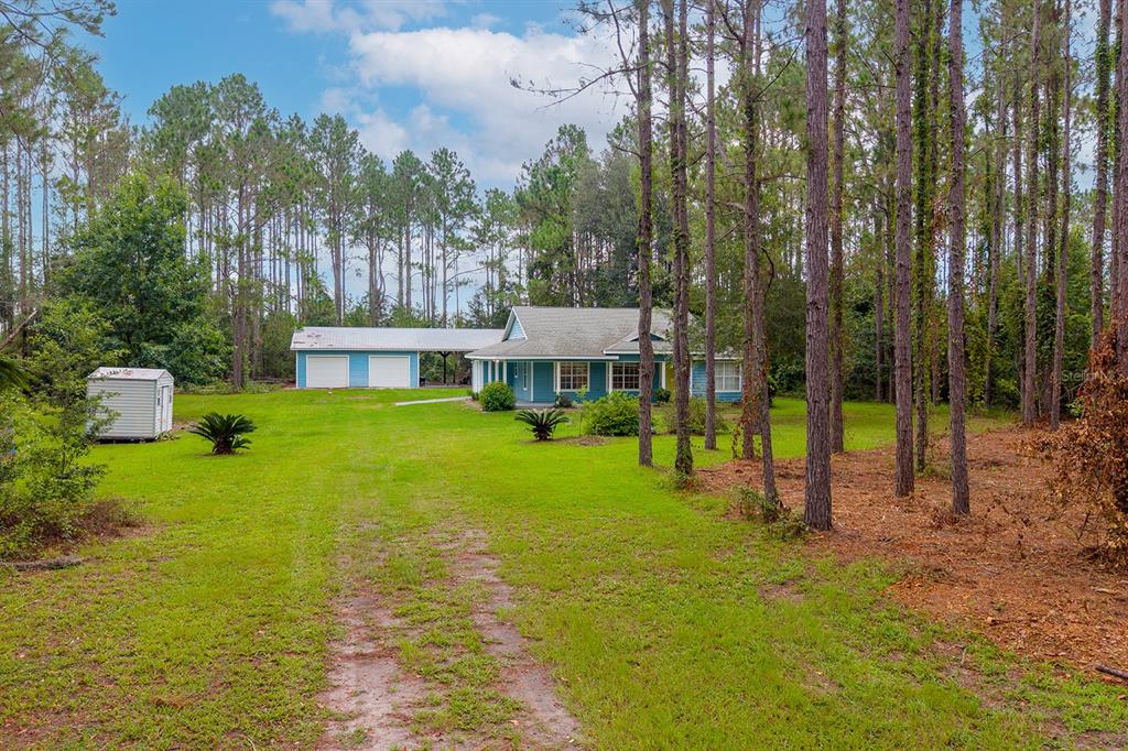A blue house with a detached garage sits on a grassy lot surrounded by trees — 670 SW 105TH STREET, TRENTON, FL
