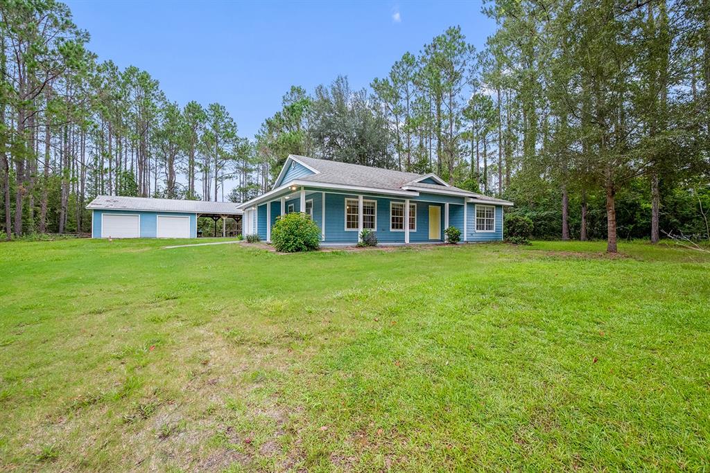 A blue single-story house with a detached garage sits on a large, grassy lawn — 670 SW 105TH STREET, TRENTON, FL