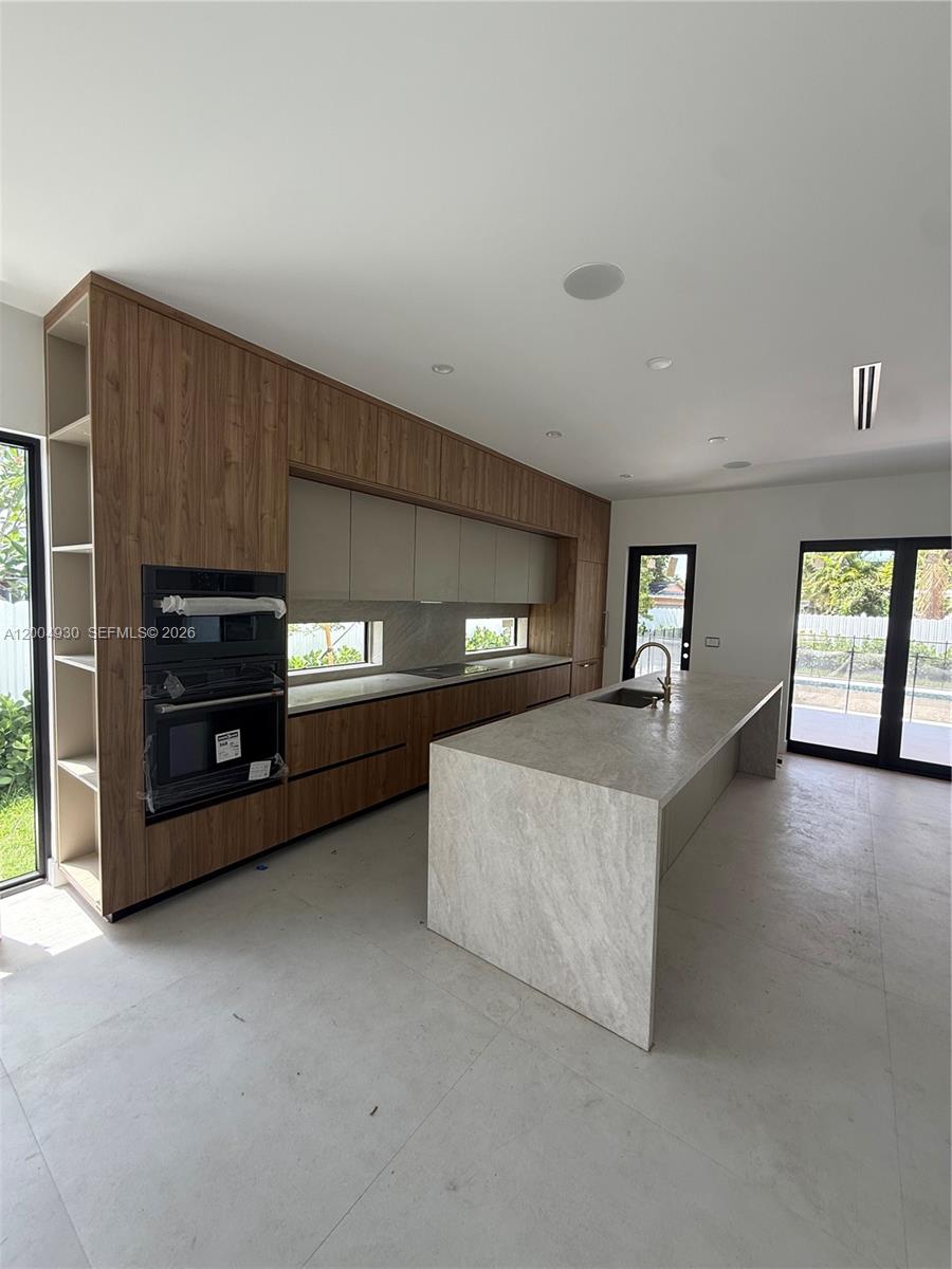 A modern kitchen features wood-toned cabinetry, a large stone island, and floor-to-ceiling windows — 6449 SW 28th St, Miami FL 33155, MIAMI, FL