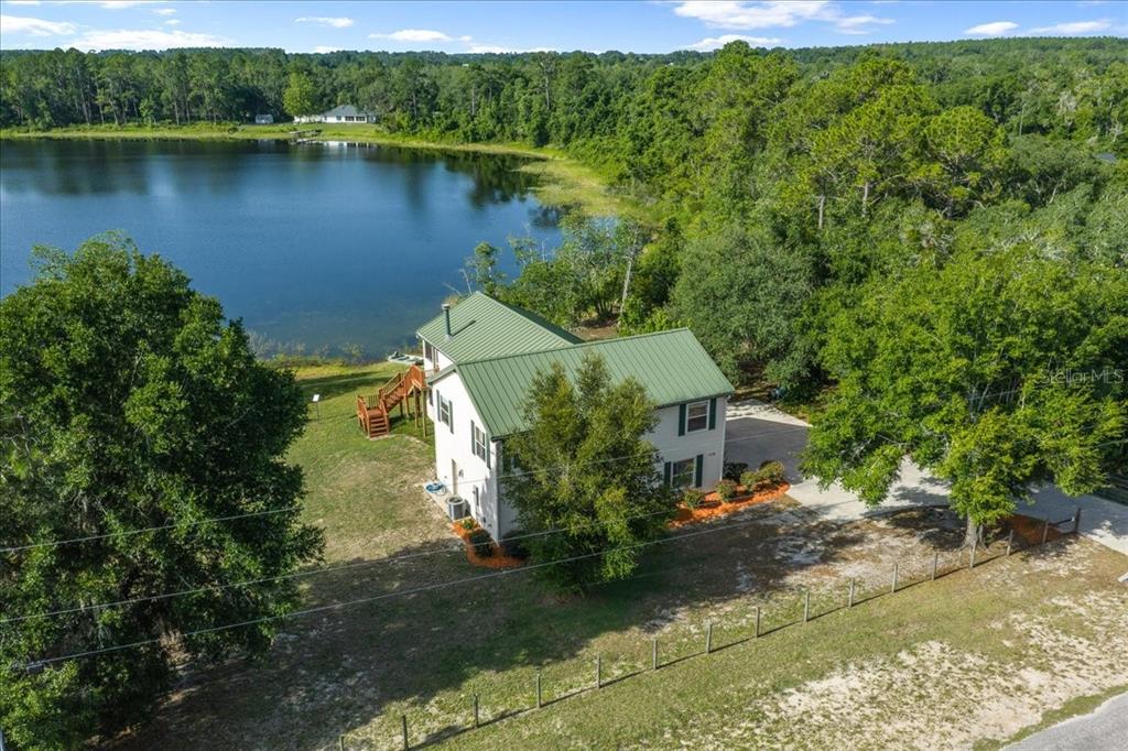 An aerial view shows a two-story house with a green metal roof beside a lake — 206 MALAUKA RADIAL, OCKLAWAHA, FL