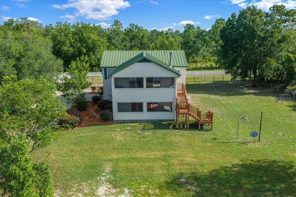 An elevated two-story house with a green metal roof and a wooden staircase — 206 MALAUKA RADIAL, OCKLAWAHA, FL