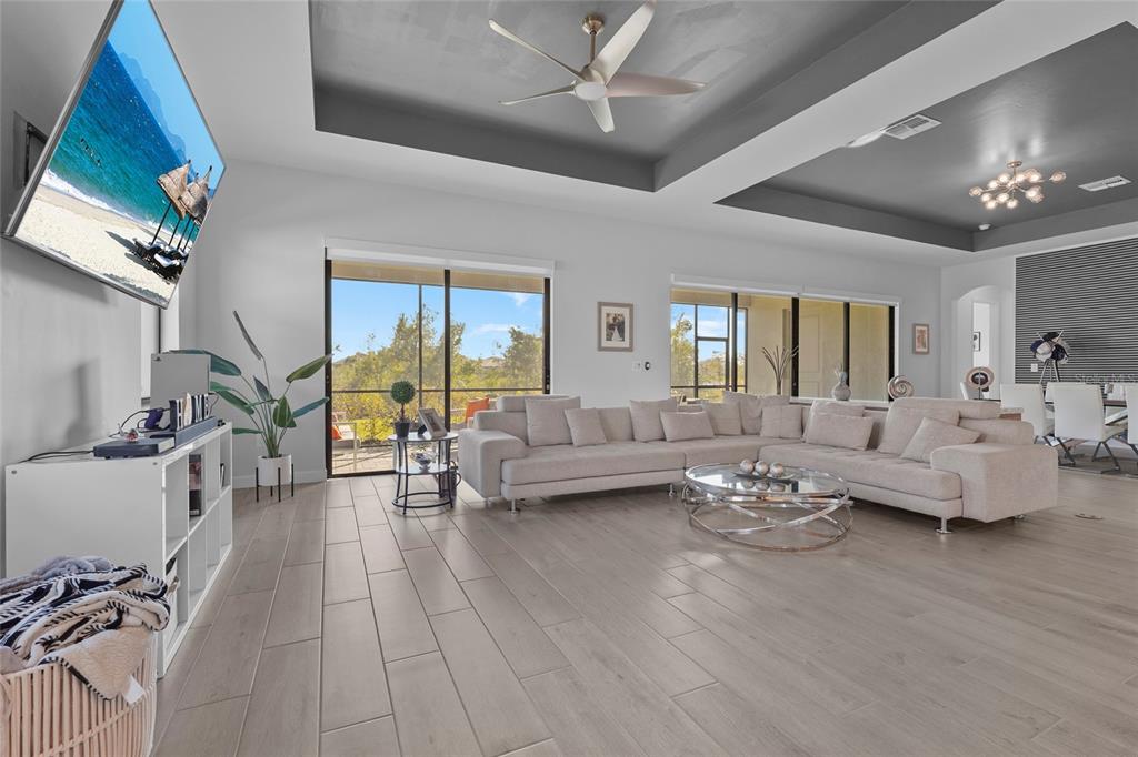 A spacious living room features light wood-look tile floors, a large sectional sofa, and tray ceilings — 15330 GOLDEN BEAM PLACE, BRADENTON, FL