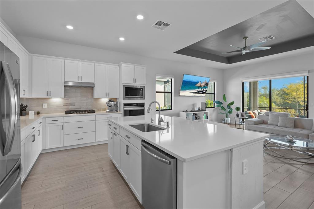 A modern kitchen with white cabinets, quartz countertops, and an island opens to a living area — 15330 GOLDEN BEAM PLACE, BRADENTON, FL