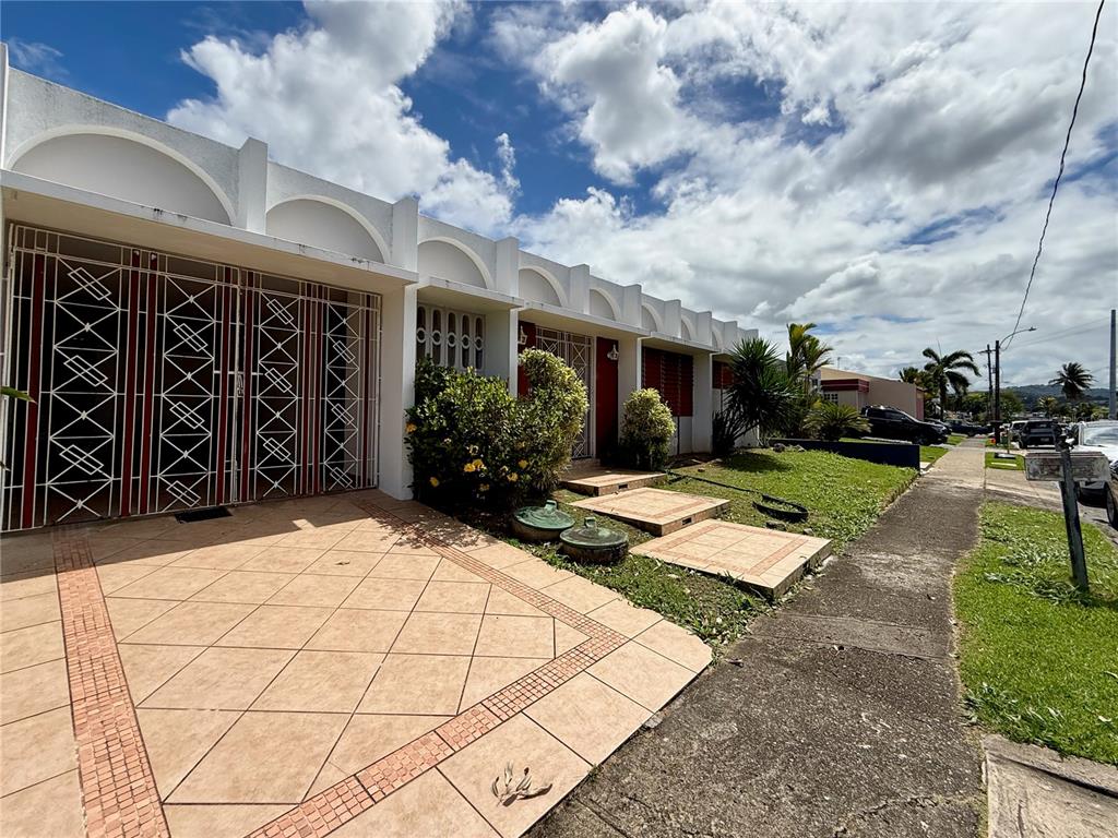A single-story house features a tiled driveway, arched roofline details, and white security gates — T-10 MCKINLEY, GUAYNABO, PR