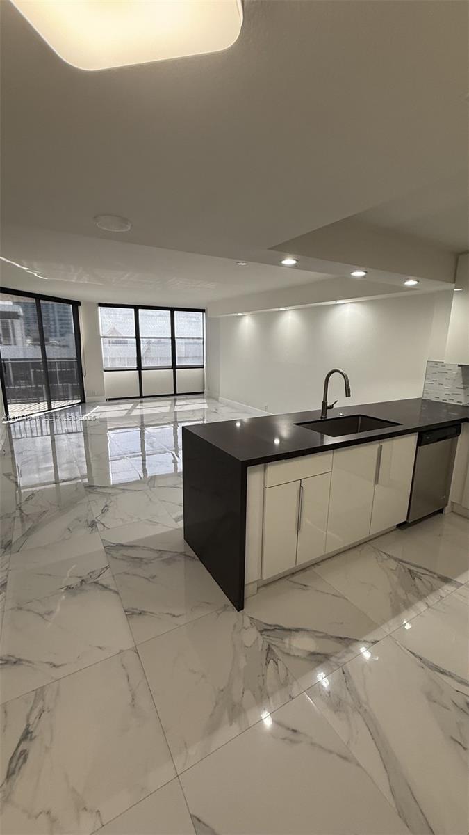 A modern kitchen with a dark countertop island overlooks a living area with marble floors — 1901 Brickell Ave # B2003, Miami FL 33129, MIAMI, FL