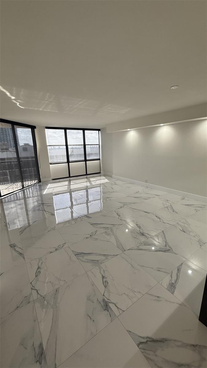 An empty room features white marble-look tile flooring, recessed lighting, and large floor-to-ceiling windows — 1901 Brickell Ave # B2003, Miami FL 33129, MIAMI, FL