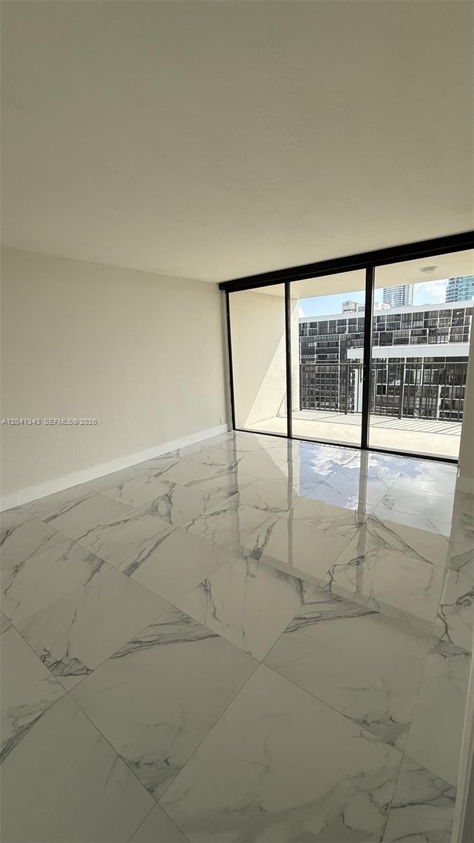 An empty room features white marble-patterned tile flooring and a large sliding glass door — 1901 Brickell Ave # B2003, Miami FL 33129, MIAMI, FL