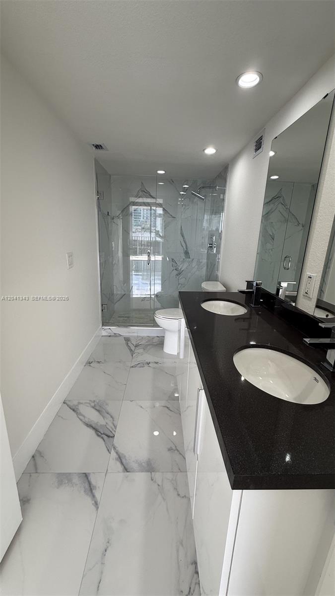 A modern bathroom features a double vanity with a black countertop and a glass-enclosed shower — 1901 Brickell Ave # B2003, Miami FL 33129, MIAMI, FL