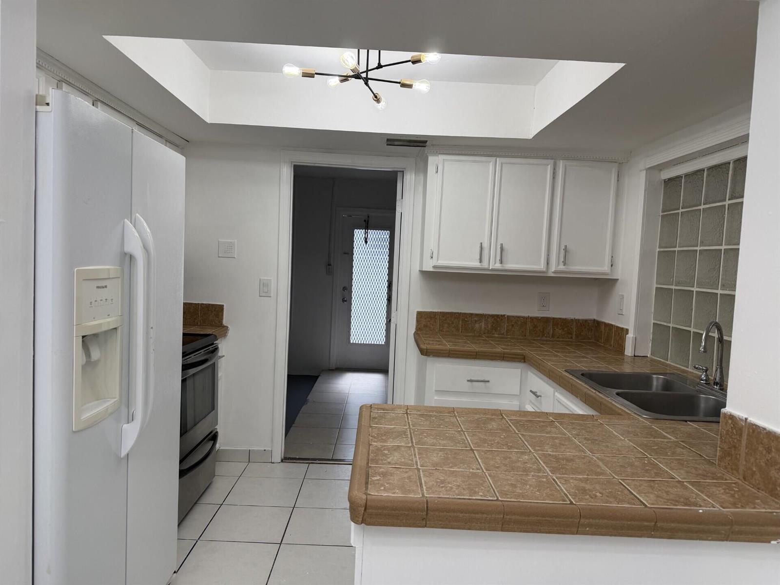 A kitchen features white cabinets, brown tile countertops, a white refrigerator, and a tray ceiling — 7315 NW 57th Place, Tamarac FL 33321, TAMARAC, FL
