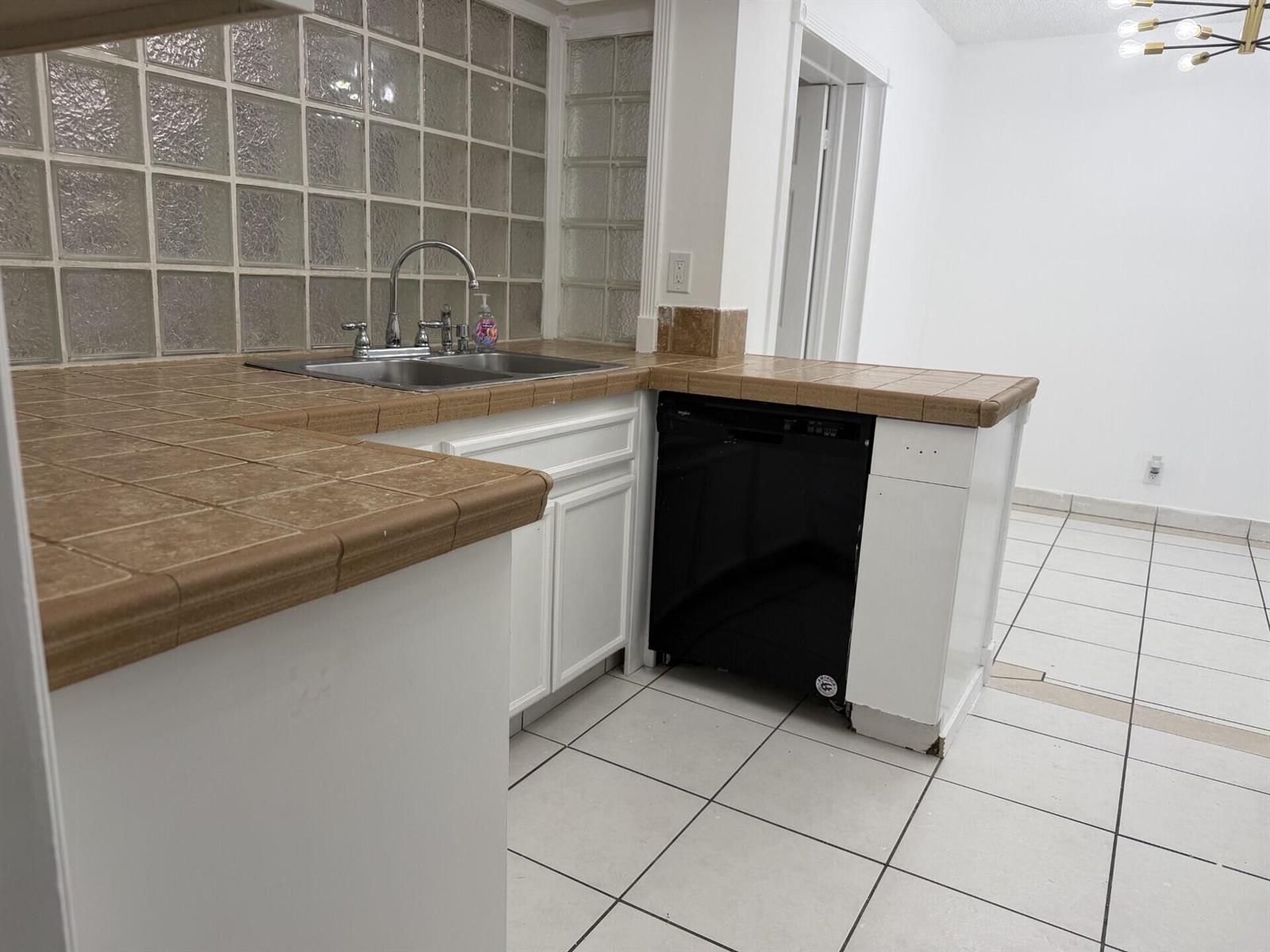 A kitchen features brown tile countertops, a black dishwasher, and a glass block backsplash — 7315 NW 57th Place, Tamarac FL 33321, TAMARAC, FL