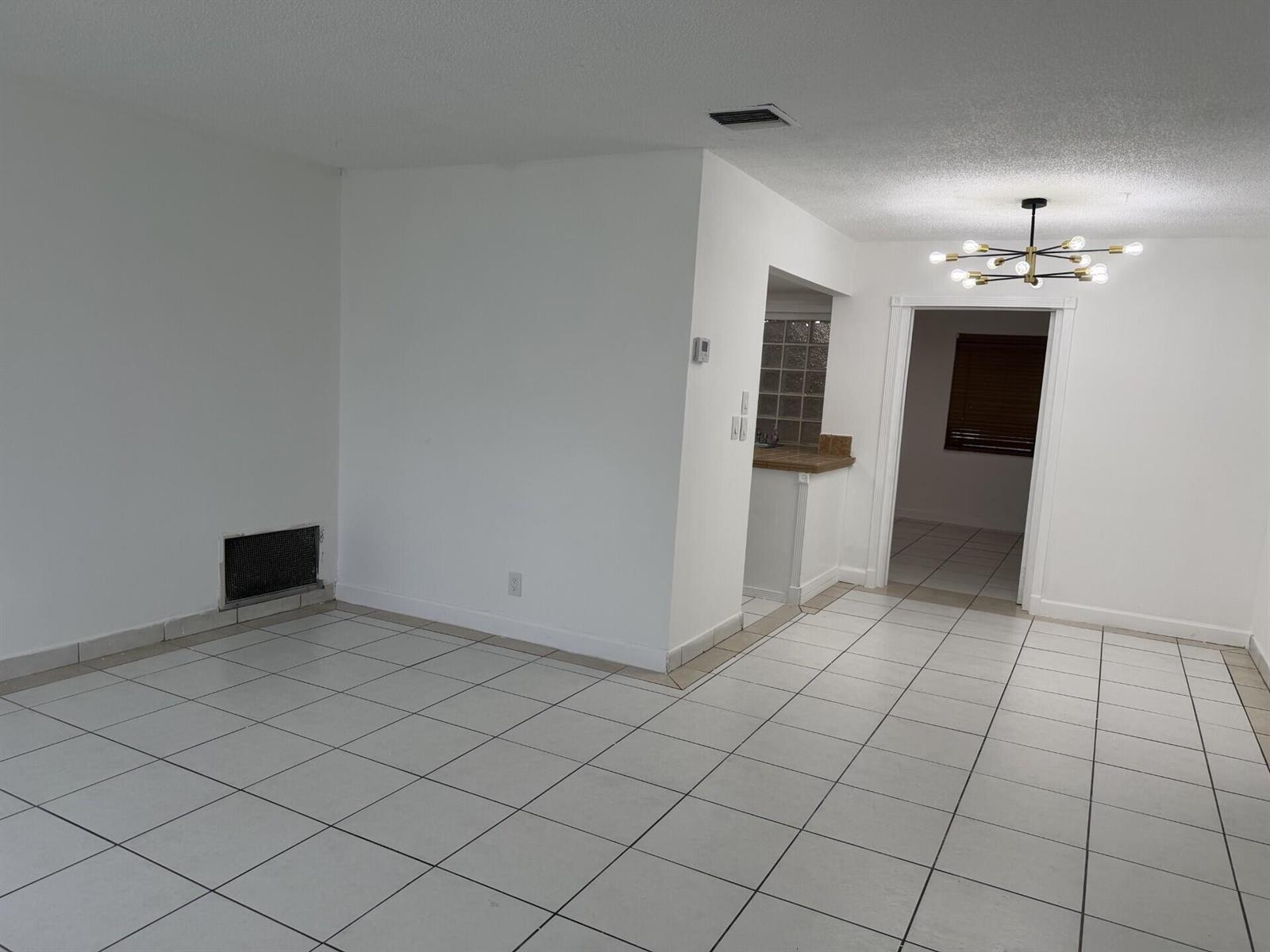 An empty room with white walls, white tiled floors, and a modern sputnik chandelier — 7315 NW 57th Place, Tamarac FL 33321, TAMARAC, FL