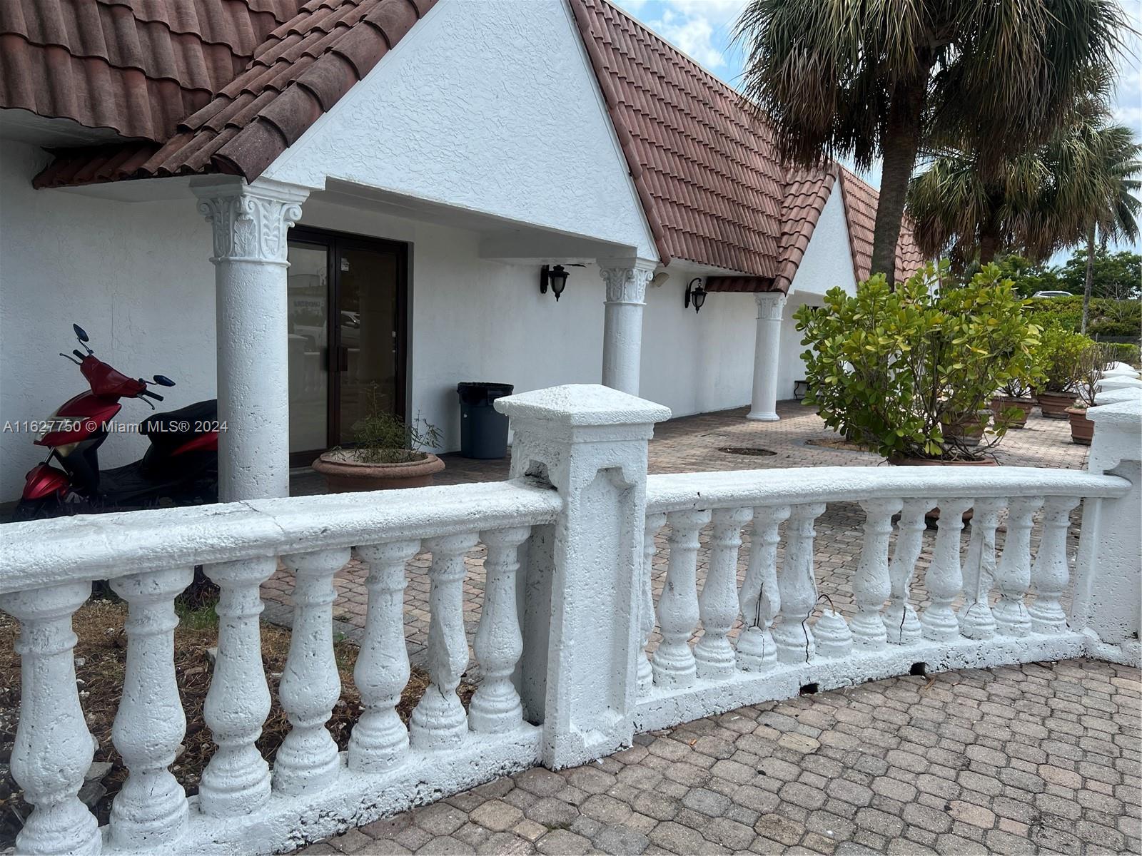 A white building with a tiled roof features a balustrade and a red scooter parked outside — 16805 NW 12th Ave, Miami Gardens FL 33169, MIAMI GARDENS, FL