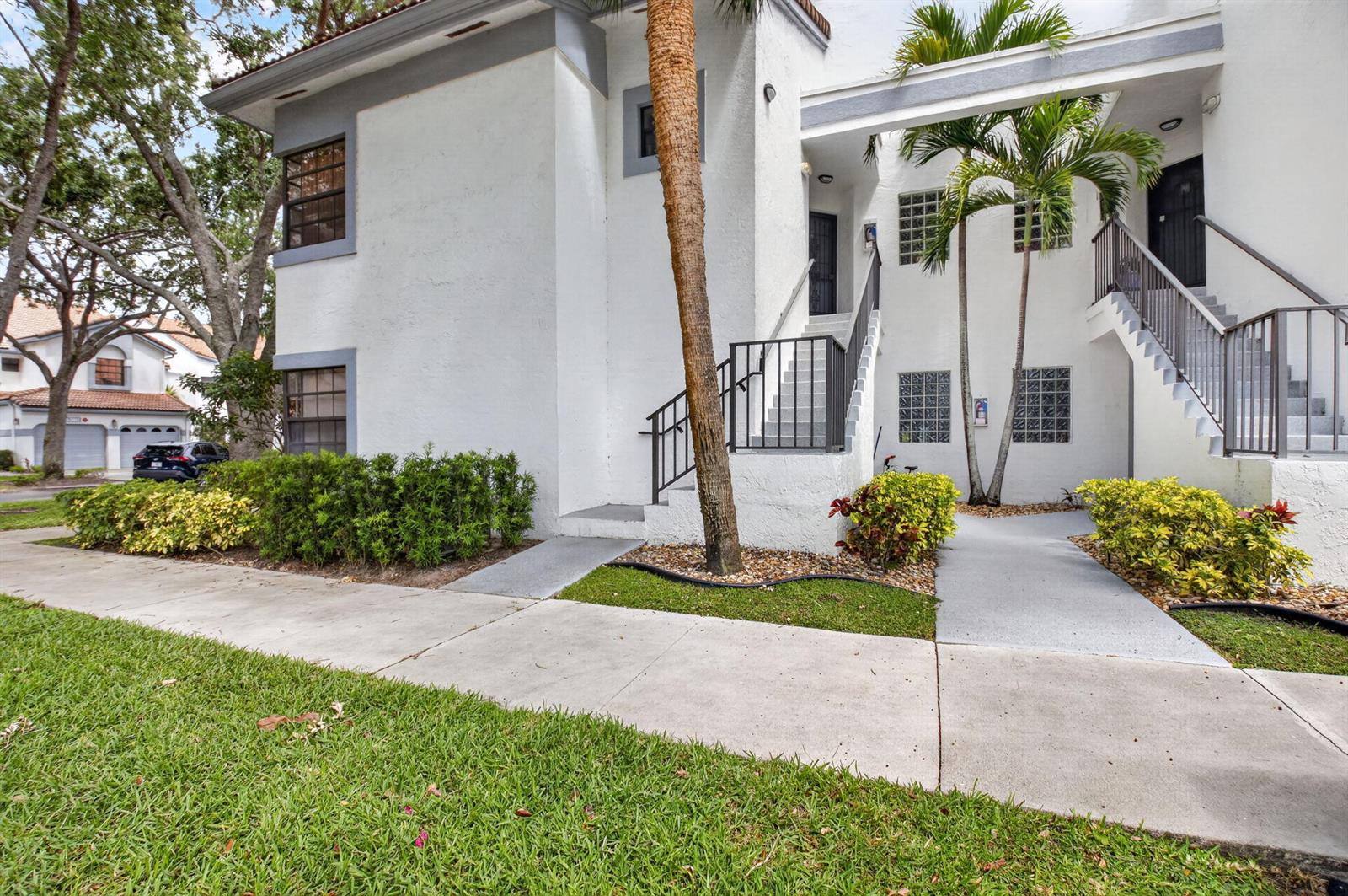 An exterior view of a two-story white stucco building with stairs and palm trees — 5430 Venetia Court, Boynton Beach FL 33437, BOYNTON BEACH, FL