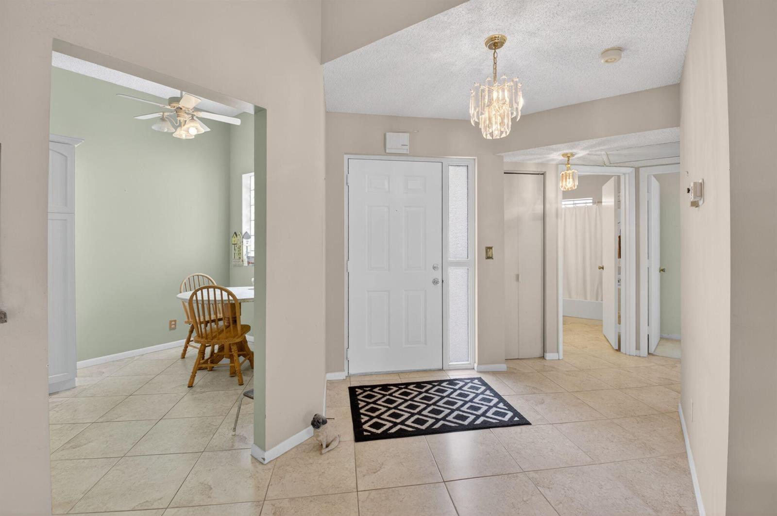 An entryway with tile flooring, a white front door, and a chandelier leads to a dining area — 5430 Venetia Court, Boynton Beach FL 33437, BOYNTON BEACH, FL