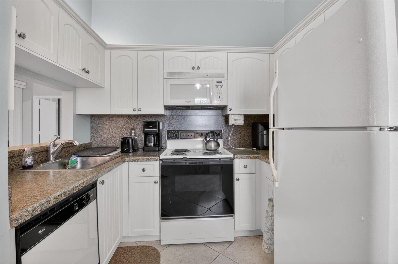 A small kitchen features white cabinets, granite countertops, a white stove, and a white refrigerator — 5430 Venetia Court, Boynton Beach FL 33437, BOYNTON BEACH, FL