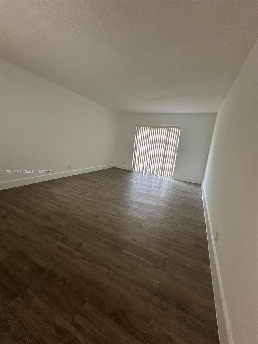An empty room features white walls, light-colored wood-look flooring, and a sliding glass door — 18101 NW 68th Ave # E210, Hialeah FL 33015, HIALEAH, FL