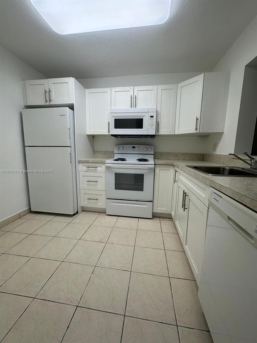 A kitchen features white cabinets, white appliances, and light-colored tile flooring — 18101 NW 68th Ave # E210, Hialeah FL 33015, HIALEAH, FL