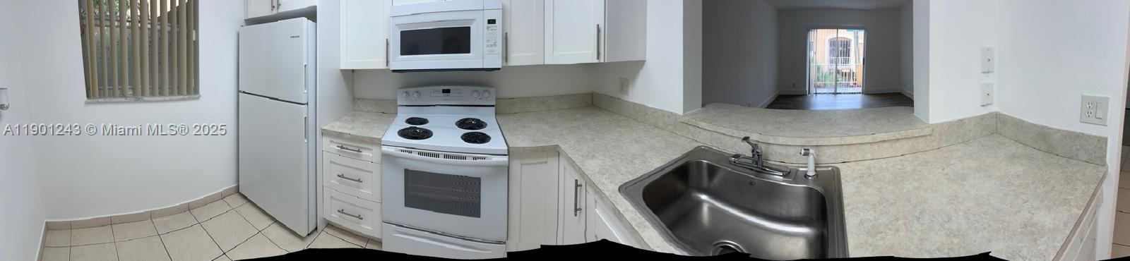 A kitchen features white appliances, light-colored cabinets, laminate countertops, and a stainless steel sink — 18101 NW 68th Ave # E210, Hialeah FL 33015, HIALEAH, FL