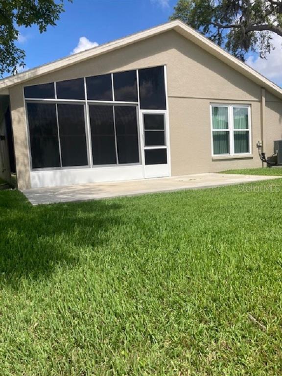 The back exterior of a house features a screened-in patio and a concrete slab — 10007 BROOKDALE DRIVE, NEW PORT RICHEY, FL