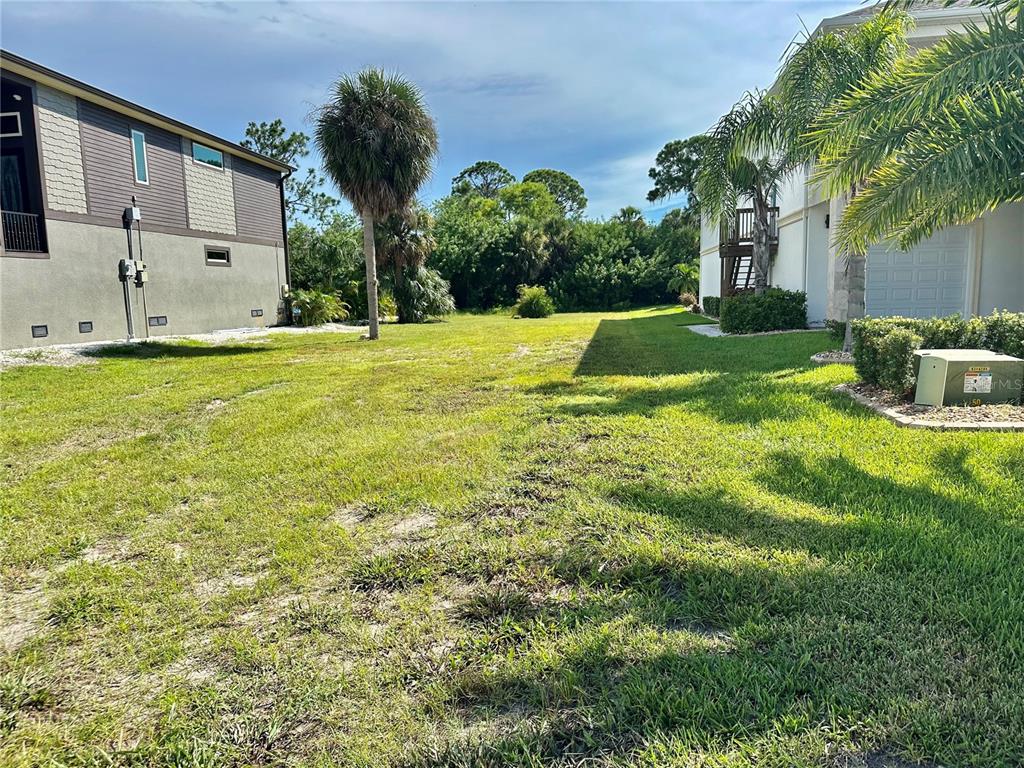 A grassy vacant lot sits between two multi-story residential buildings under a blue sky — 0 EGRETS PLACE, NEW PORT RICHEY, FL