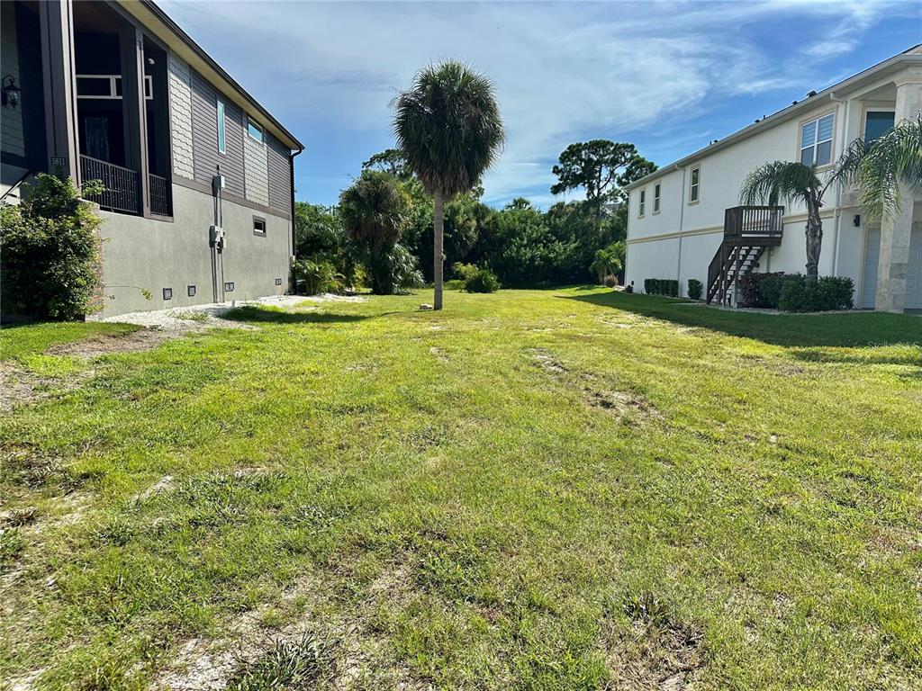 A grassy vacant lot sits between two multi-story residential buildings under a blue sky — 0 EGRETS PLACE, NEW PORT RICHEY, FL